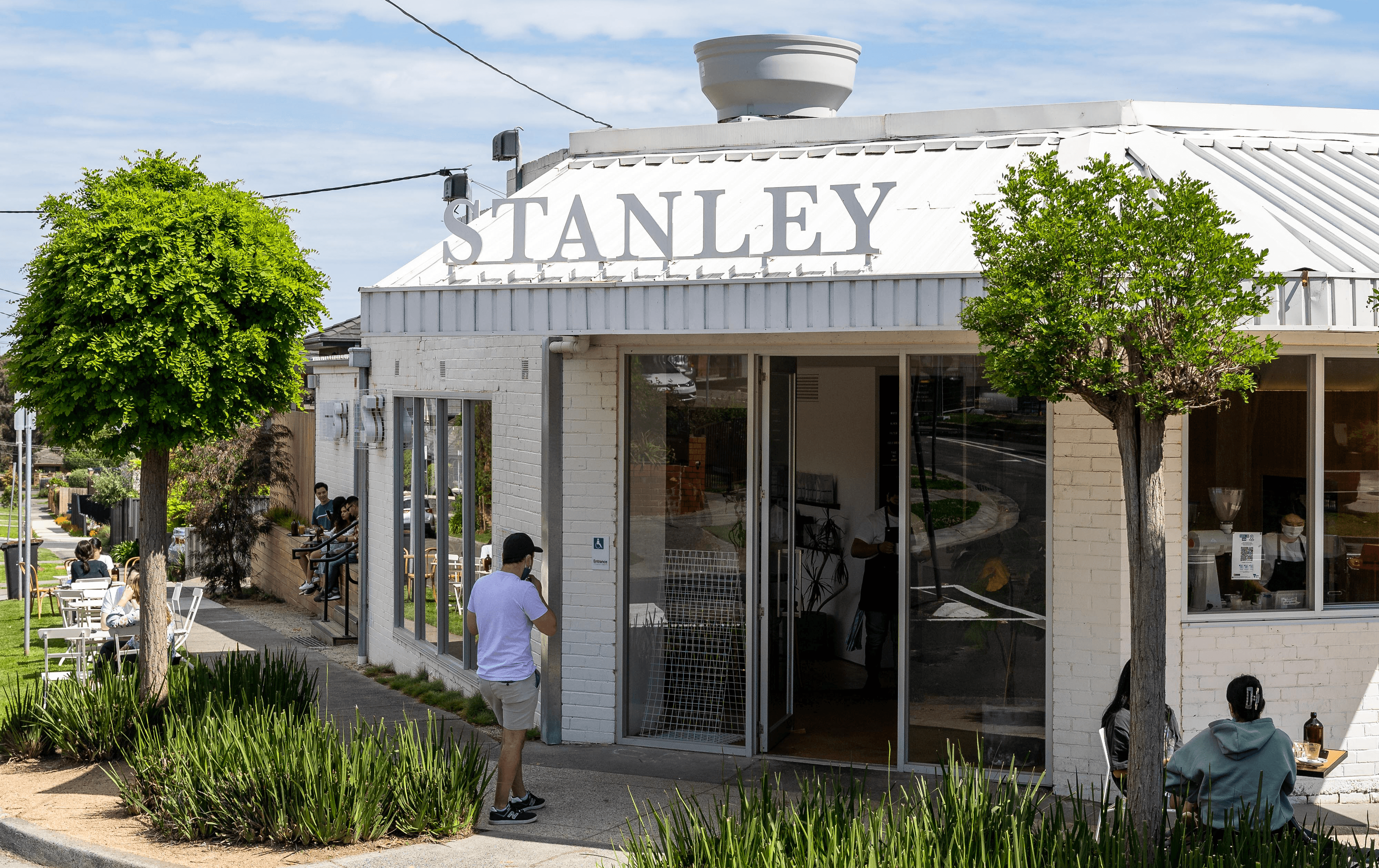 A white cafe on a corner with green leafy trees out front.